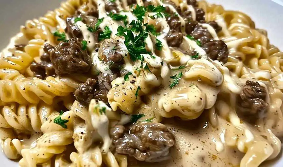Ground beef browning in skillet with garlic for rotini pasta dish

