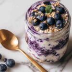 Creamy blueberry cheesecake overnight oats topped with fresh berries in mason jar