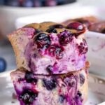 Slice of blueberry cottage cheese breakfast bake on white plate with maple syrup drizzle and fork
