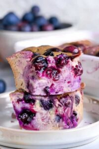 Slice of blueberry cottage cheese breakfast bake on white plate with maple syrup drizzle and fork