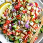 Hands mixing Greek quinoa salad with lemon dressing in large mixing bowl
