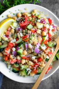Hands mixing Greek quinoa salad with lemon dressing in large mixing bowl