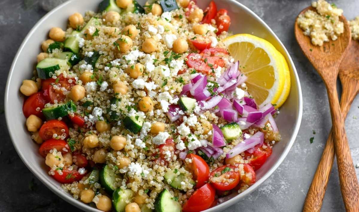 Hands mixing Greek quinoa salad with lemon dressing in large mixing bowl