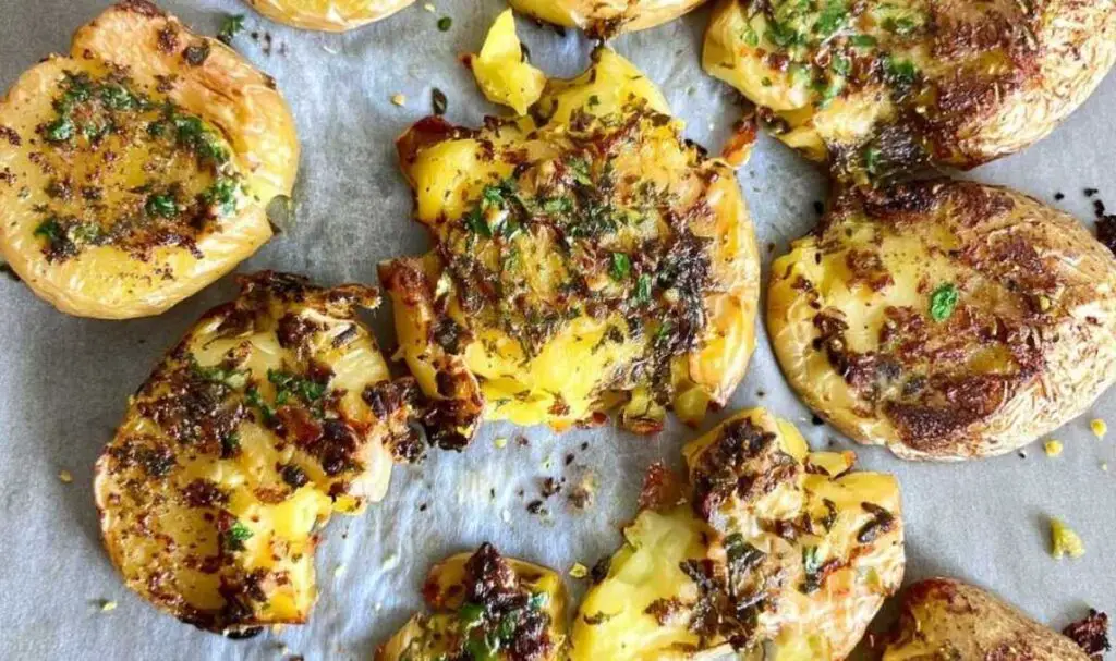 Hands smashing boiled baby potatoes with glass on baking sheet for lemon herb smashed potatoes