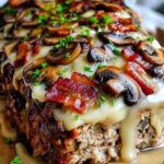 Sliced bacon mushroom swiss cheese meatloaf on white plate with mashed potatoes and green beans