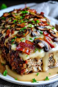 Sliced bacon mushroom swiss cheese meatloaf on white plate with mashed potatoes and green beans