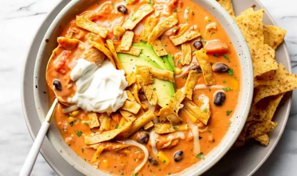 Creamy chicken tortilla soup in white bowl topped with avocado and tortilla strips