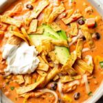 Two bowls of creamy chicken tortilla soup with colorful toppings and lime wedges