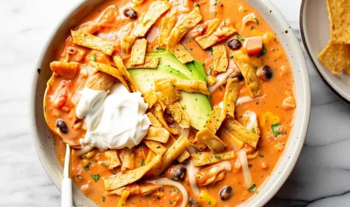 Two bowls of creamy chicken tortilla soup with colorful toppings and lime wedges