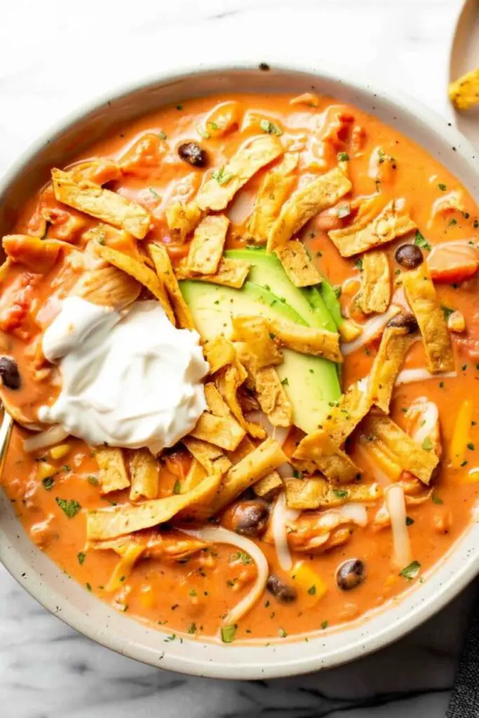Two bowls of creamy chicken tortilla soup with colorful toppings and lime wedges
