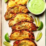 Crispy black bean tacos on a white plate with lime wedges and cilantro
