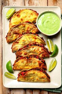 Crispy black bean tacos on a white plate with lime wedges and cilantro