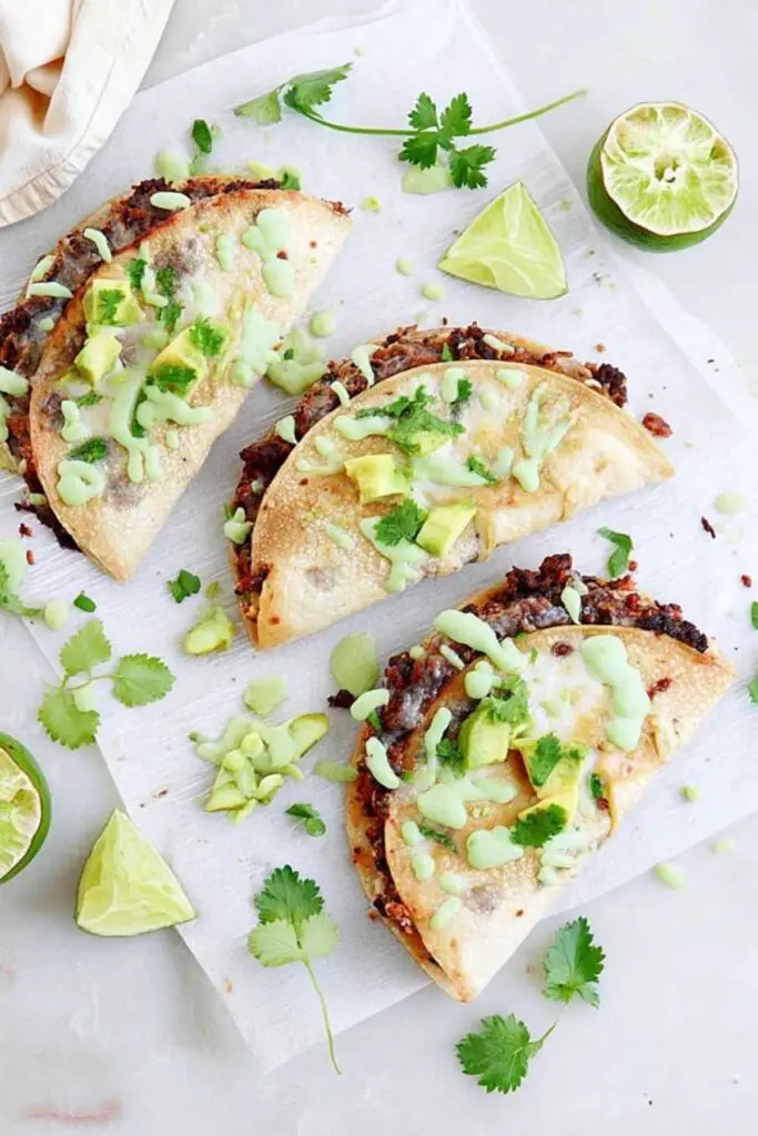 Crispy smashed black bean tacos on white plate with lime cilantro sauce