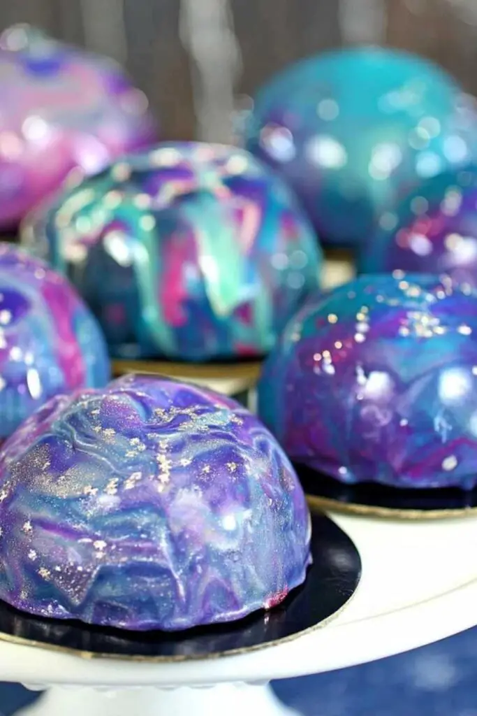 Pouring colorful mirror glaze over Galaxy Mousse Cakes creating cosmic effect