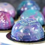 Pouring colorful mirror glaze over Galaxy Mousse Cakes creating cosmic effect