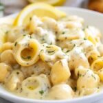 Creamy garlic butter pasta in white bowl with fresh herbs and Parmesan cheese