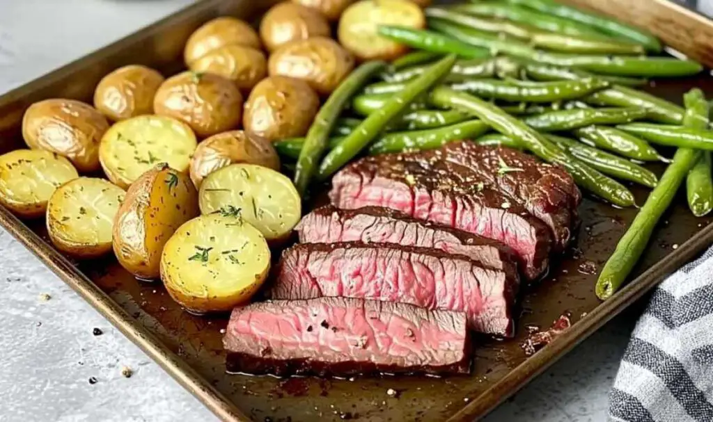 Sheet pan with roasted potatoes and steak cooking in oven for herbed steak sheet pan dinner