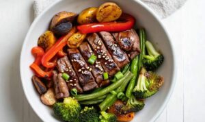 Raw marinated beef and fresh vegetables arranged on sheet pan before roasting