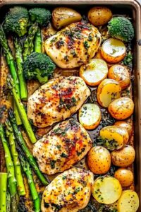 Raw chicken and vegetables arranged on sheet pan before roasting with garlic butter