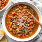 Hearty minestrone lentil soup in white bowl with parmesan cheese and crusty bread
