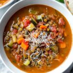 Hearty minestrone lentil soup in white bowl with parmesan cheese and crusty bread