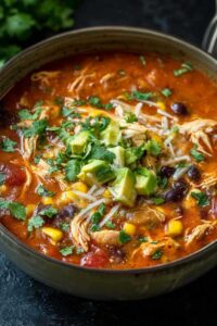 Bowl of chicken enchilada soup topped with cheese, sour cream, and cilantro