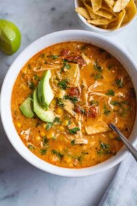 Creamy chicken tortilla soup in white bowl topped with tortilla strips and cheese