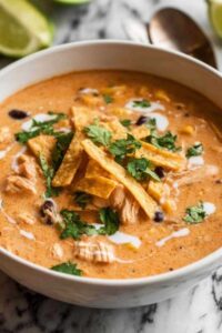 Creamy chicken tortilla soup in white bowl topped with cheese, cilantro, and tortilla strips