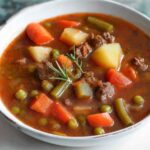 Old-fashioned vegetable beef soup in white bowl with crusty bread