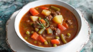 Old-fashioned vegetable beef soup in white bowl with crusty bread