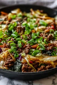 Asian-inspired beef and cabbage skillet in cast iron pan with sesame seeds and green onions