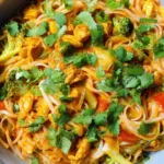 Bowl of coconut curry chicken rice noodles with broccoli and carrots topped with cilantro
