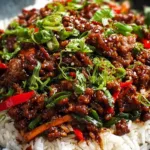 Crispy chilli beef rice with spring onions and sesame seeds in white bowl
