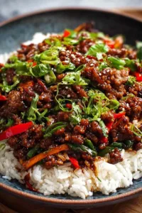 Crispy chilli beef rice with spring onions and sesame seeds in white bowl