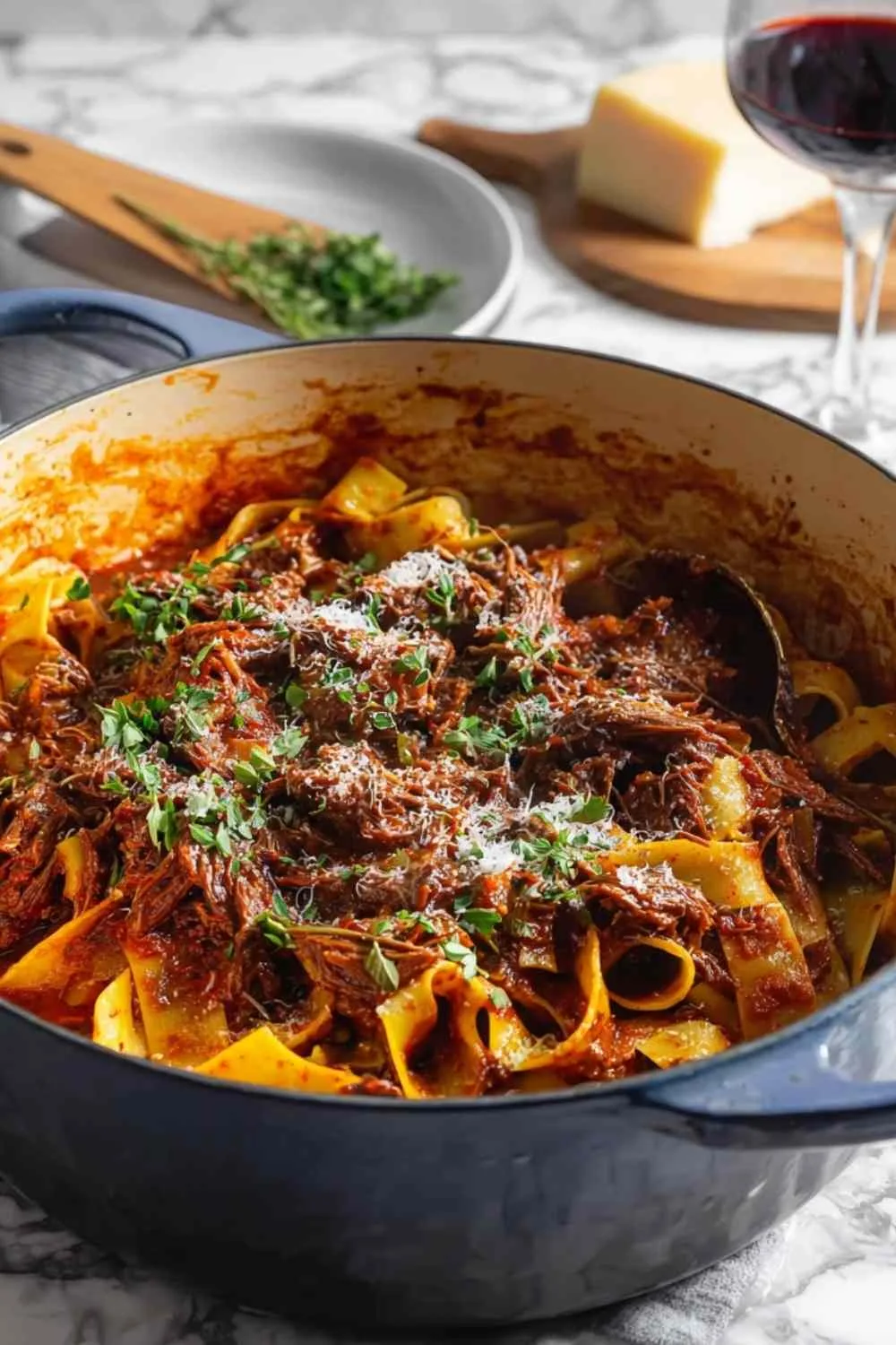 Dutch oven short rib ragu with pappardelle pasta topped with parmesan cheese
