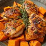 Maple glazed chicken with sweet potatoes served on white dinner plate with fresh herbs
