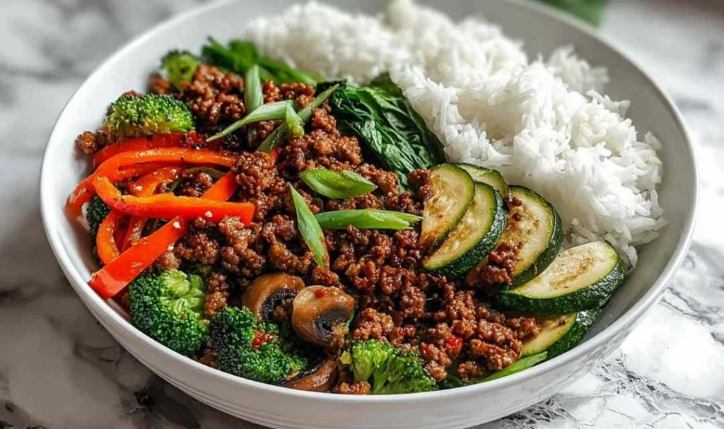 Spicy ground beef stir-fry bowl with colorful vegetables and steamed rice in white bowl