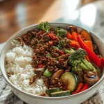 Spicy ground beef stir-fry bowl with colorful vegetables and steamed rice in white bowl