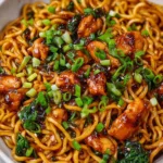 Sticky garlic chicken noodles in white bowl with chopsticks and sesame seeds