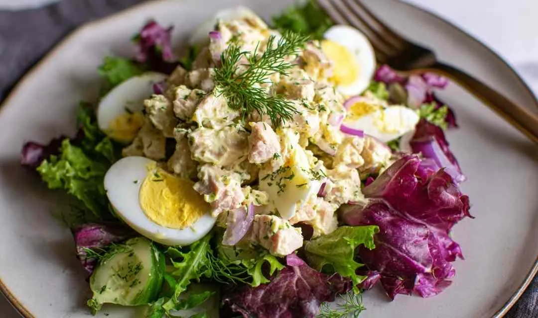Tuna egg salad in white bowl with fork showing chunky texture
