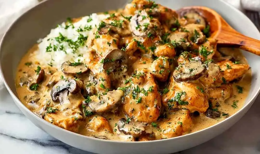 Creamy chicken stroganoff served over egg noodles in white bowl