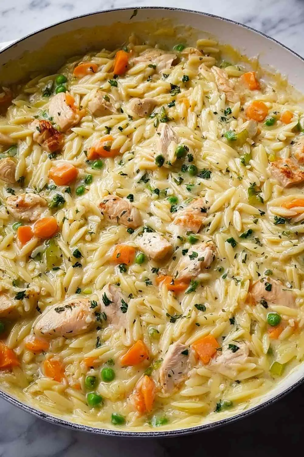 Bowl of creamy chicken orzo garnished with parsley on rustic table