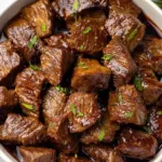 Slow cooker filled with steak bites onions and garlic in au jus gravy