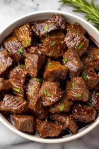 Slow cooker filled with steak bites onions and garlic in au jus gravy
