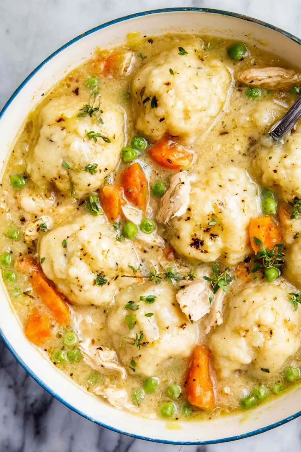 Bowl of easy chicken and dumplings with spoon and fresh thyme garnish