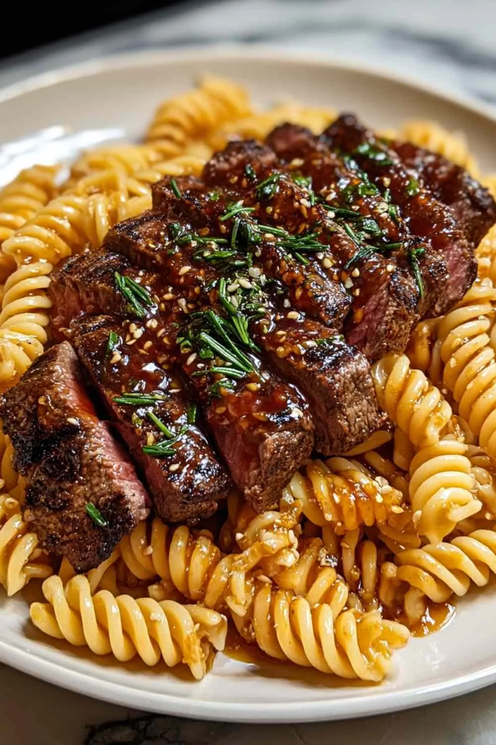 Rotini pasta being stirred into honey garlic steak in skillet