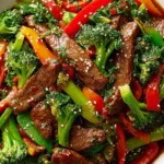 Beef stir fry with fresh vegetables served over steamed jasmine rice in a white bowl