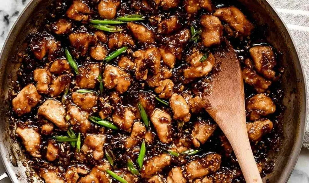 Bourbon Chicken cooking in a skillet with sticky brown sauce.