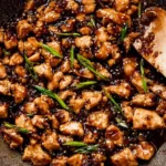 Bourbon Chicken cooking in a skillet with sticky brown sauce.