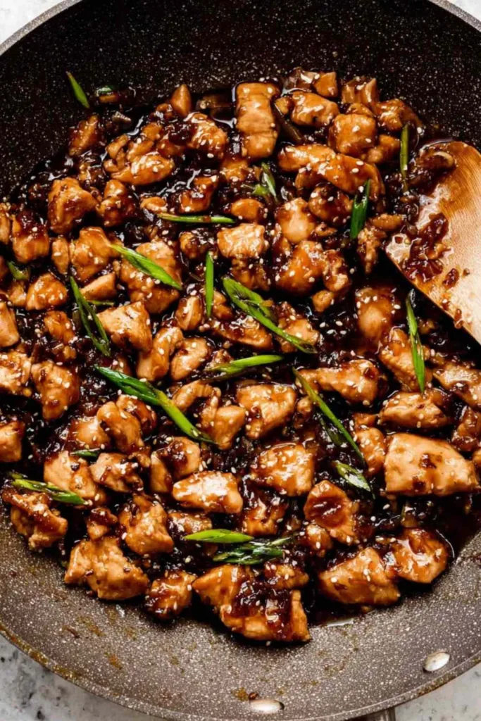 Bourbon Chicken cooking in a skillet with sticky brown sauce.